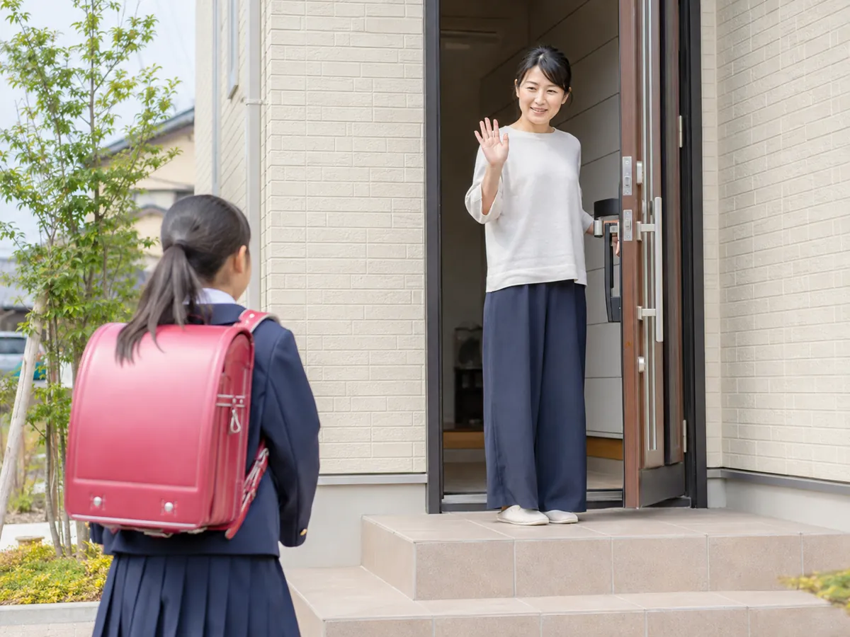 玄関先で、学校から帰ってきた子どもを迎える母親